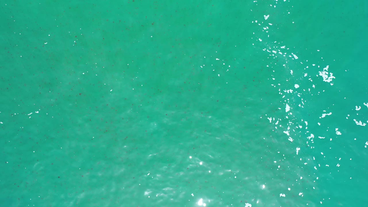 Turquoise sea surface in Los Cabos, Mexico, with a brighter vertical scatter of sun glints near the center and no visible people.