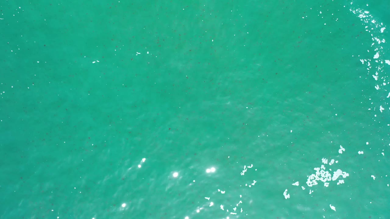 Clear teal ocean surface in Los Cabos, Mexico, with a diagonal cluster of bright wave highlights and no visible people.