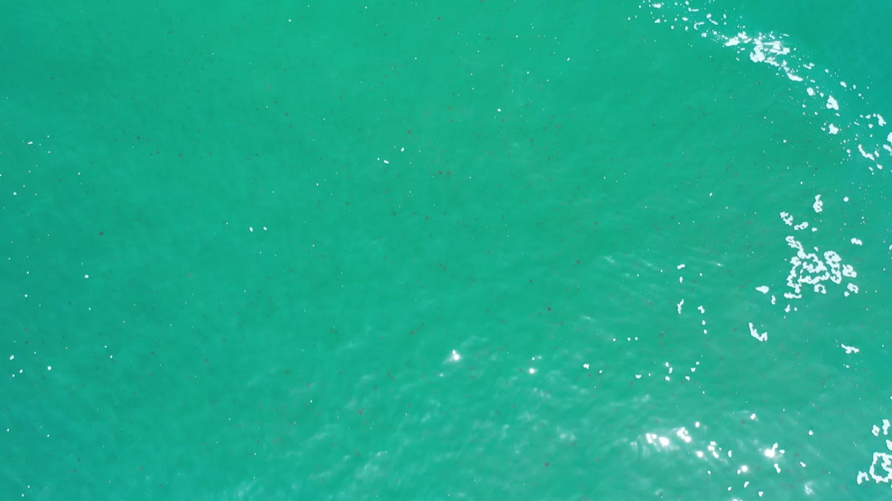 Bright turquoise water with scattered white foam near the upper right.