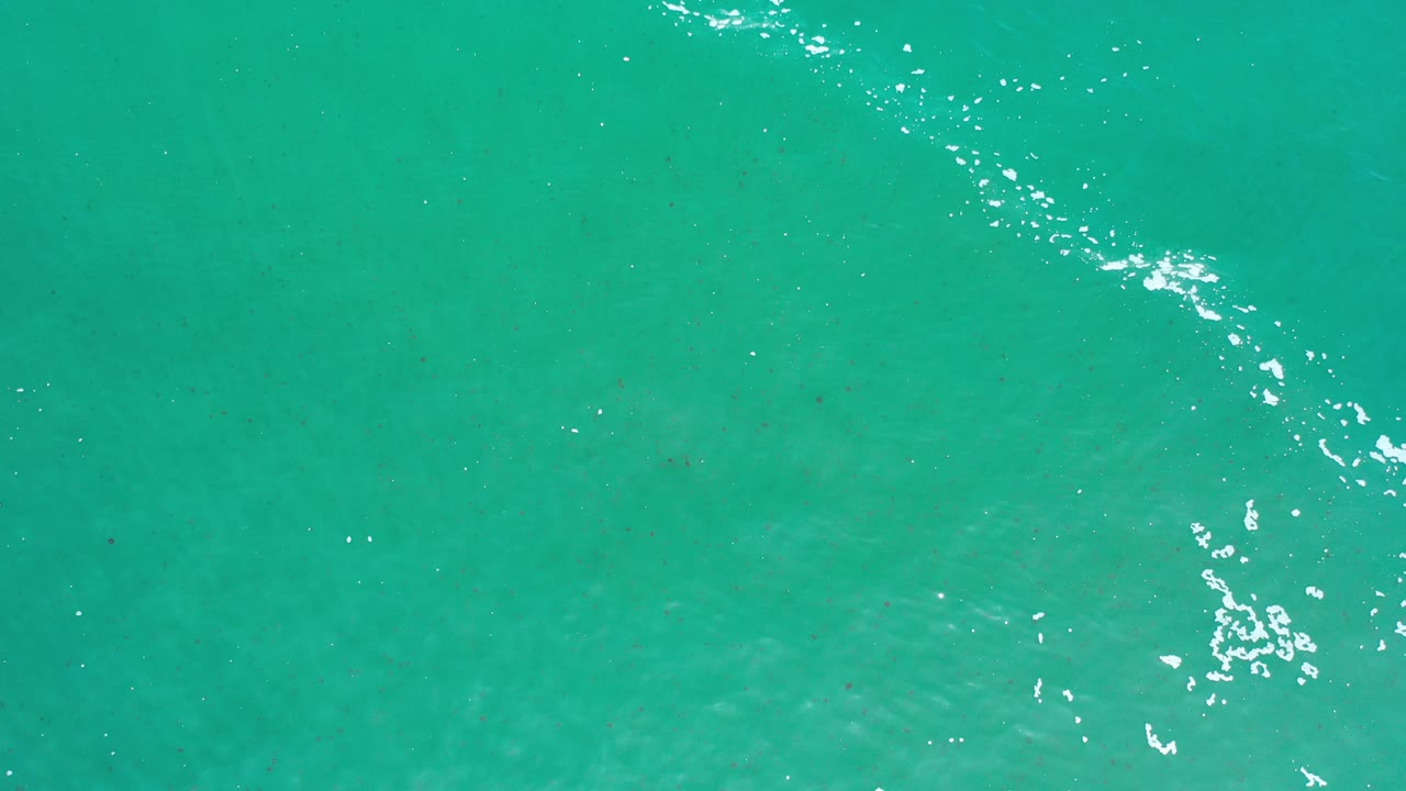 Overhead view of green-turquoise sea water in Los Cabos, Mexico, with scattered white foam near the upper right and no visible people.