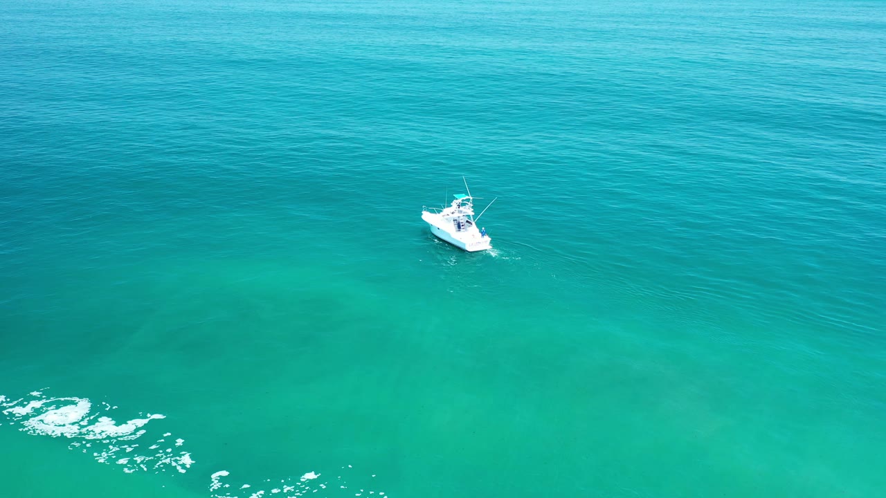 Aerial frame of the white boat on open Los Cabos water, slightly farther right against blue-green ripples, with no visible people.