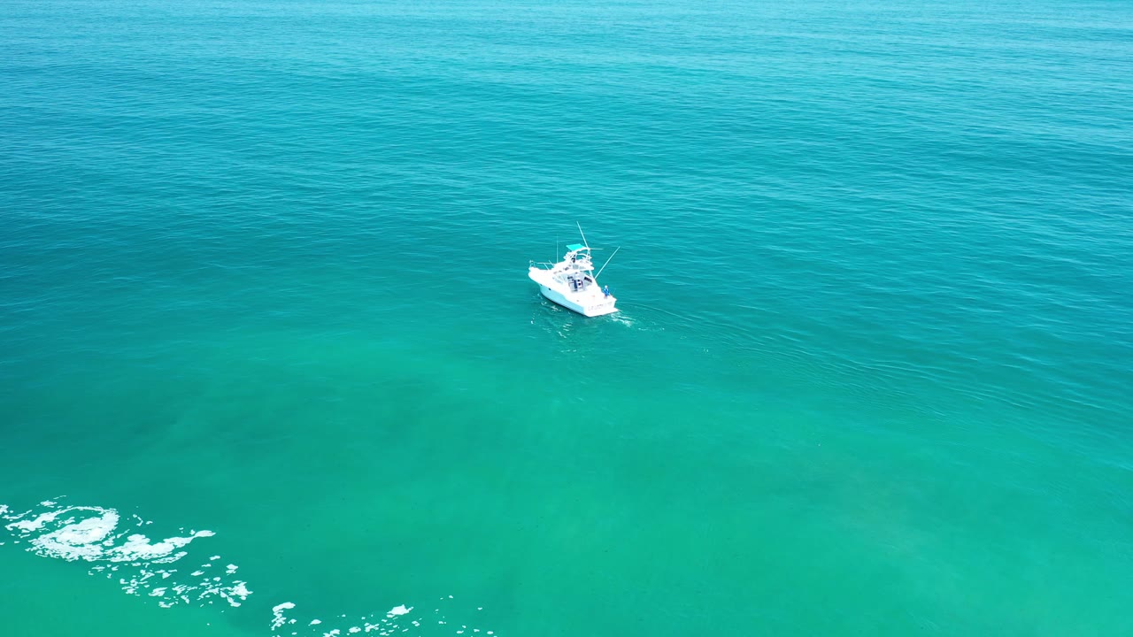 Small white boat on blue and teal water with bright glare lower left.