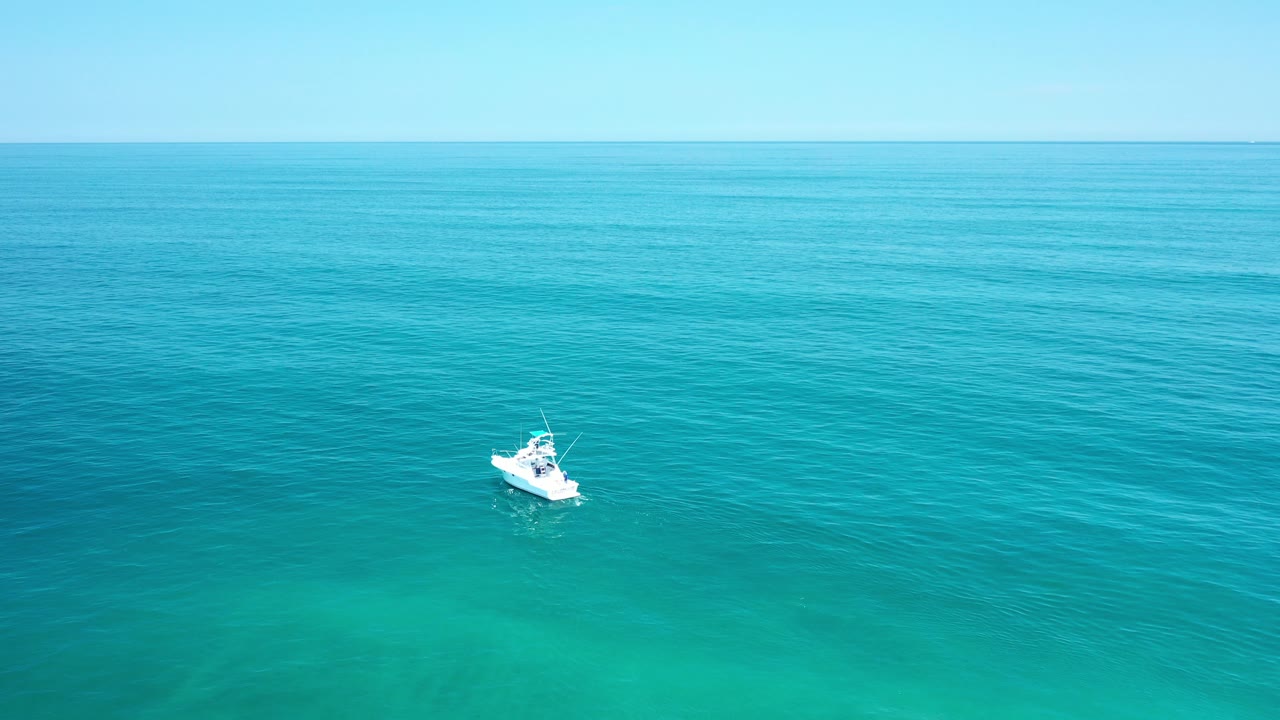 Small white boat on turquoise ocean beneath a pale sky