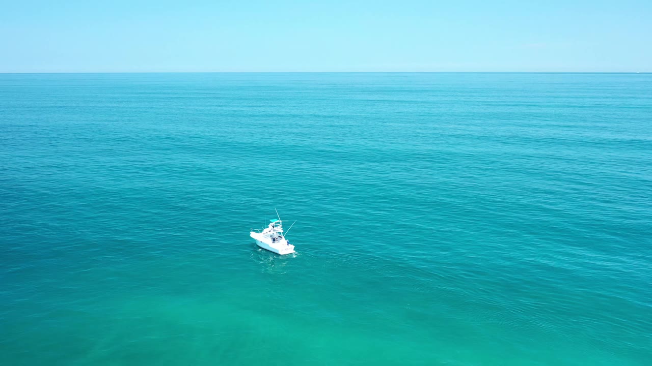 One second in, the white boat remains small against the Los Cabos ocean, surrounded by green-blue water and a level horizon, with no visible people.