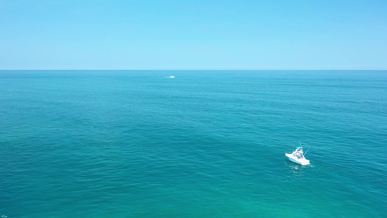 Aerial Los Cabos ocean frame with the white motorboat slightly lower in the composition and the horizon stretching across the background, with no visible people.