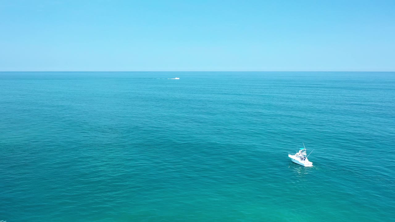 Distant white boat on calm ocean with clear blue sky.