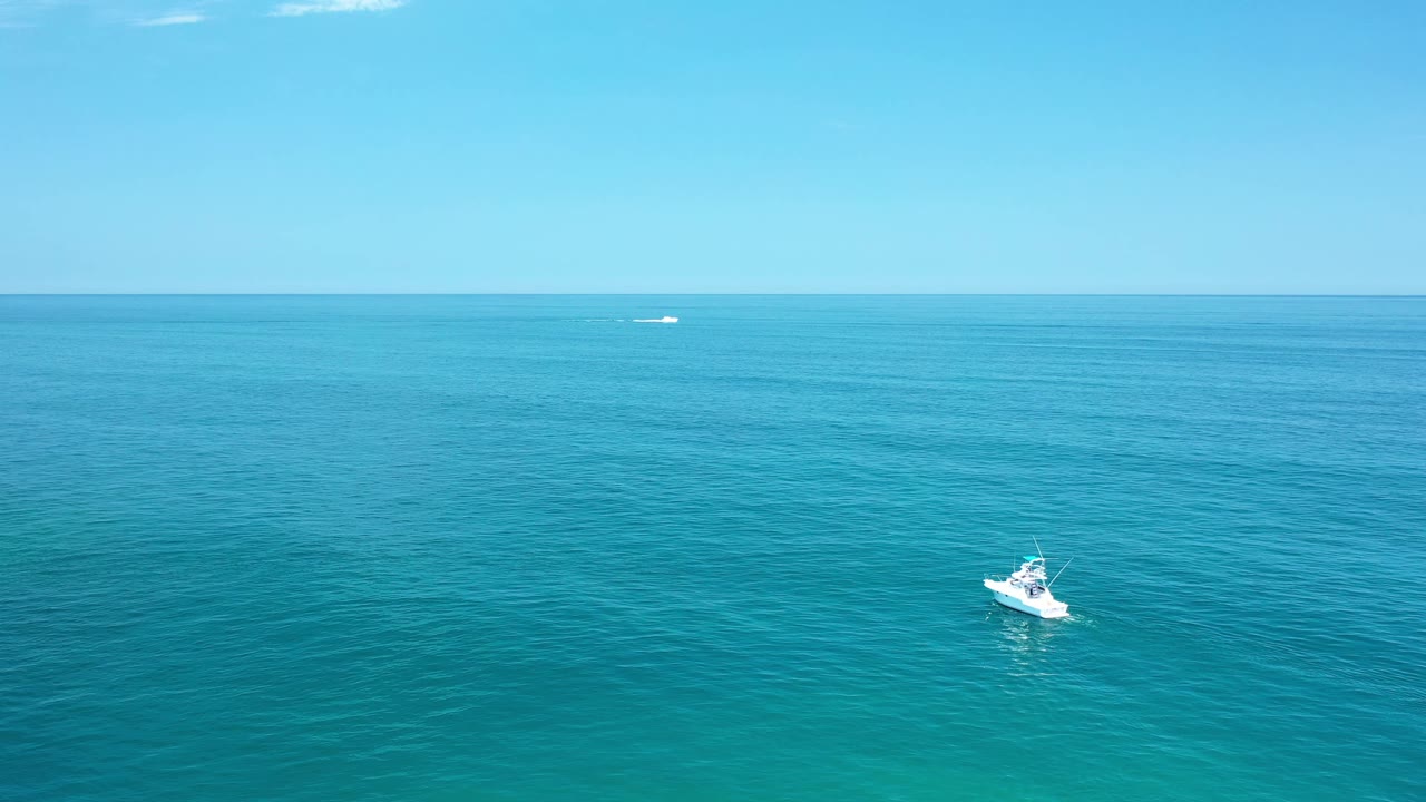 At 0:01, the white fishing boat remains low in the composition on calm turquoise water in Los Cabos, Mexico, with the horizon steady and no visible people.
