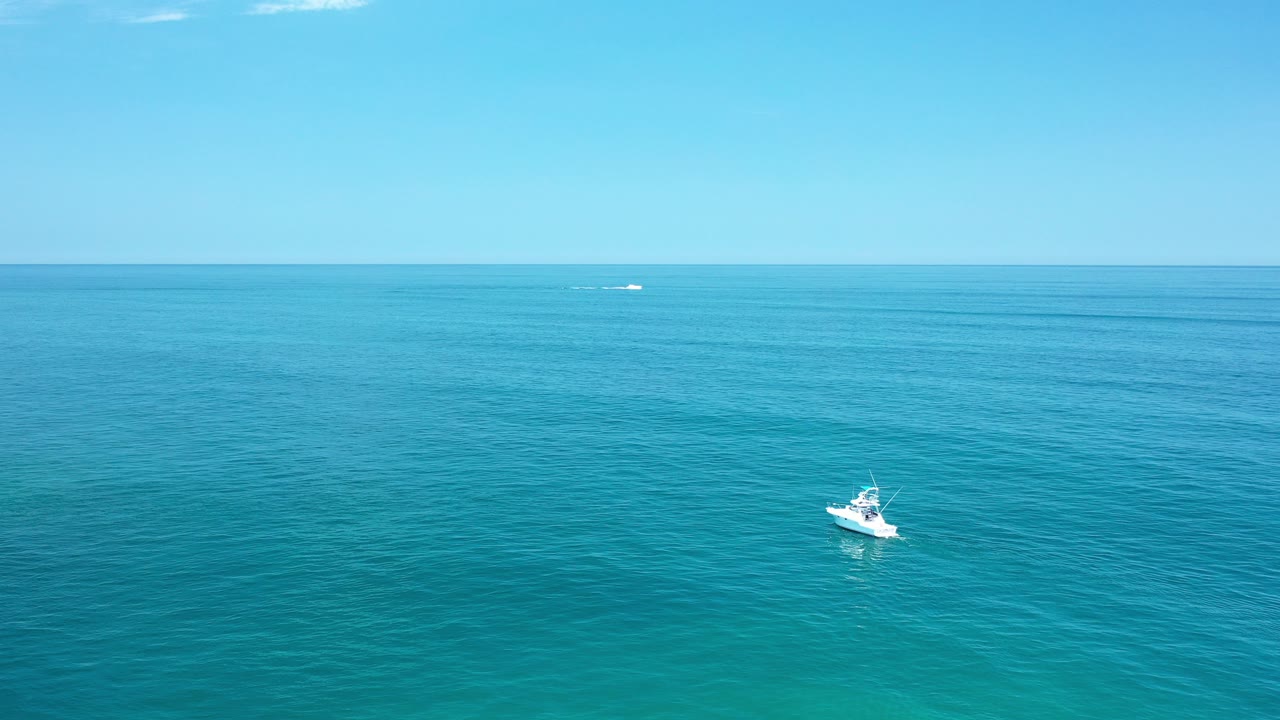 Wide aerial view in Los Cabos, Mexico with a small white boat below the horizon on calm turquoise water and no visible people.
