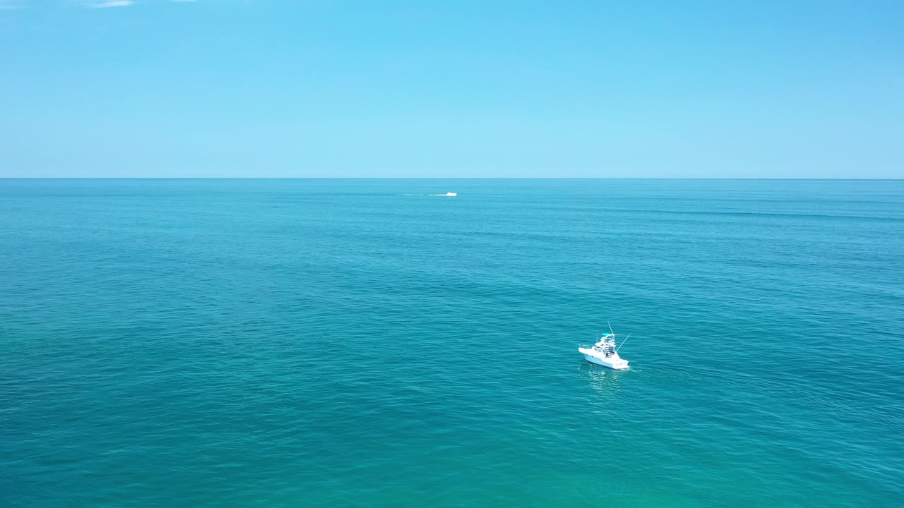 White boat on calm sea with blue sky and distant water marks.