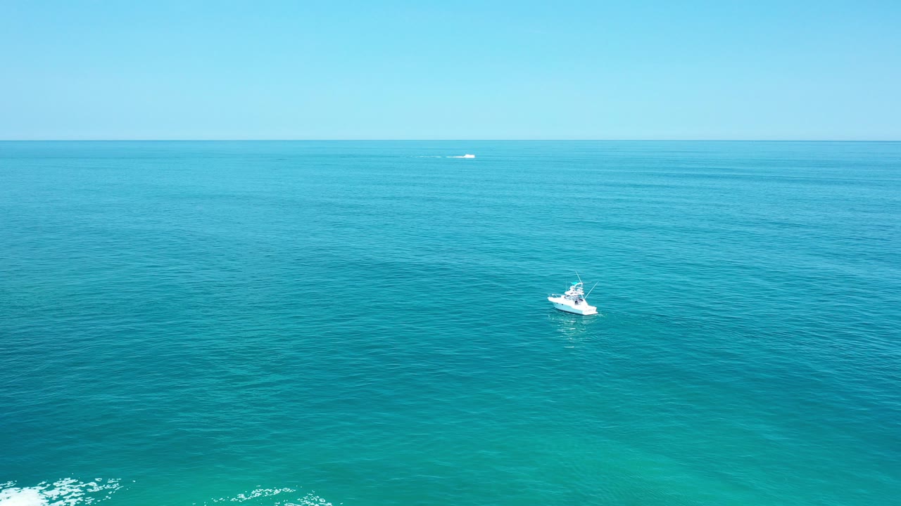 At the start of the Los Cabos, Mexico clip, a small white boat sits left of center on blue-green open water with a pale sky above and no clearly visible people.