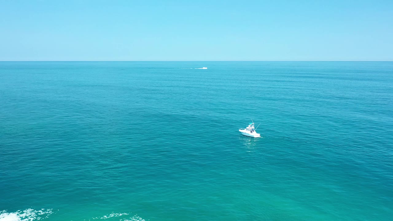 One second in, the small white boat appears nearer the center of the Los Cabos ocean view, with subtle ripples across the water and no clearly visible people.