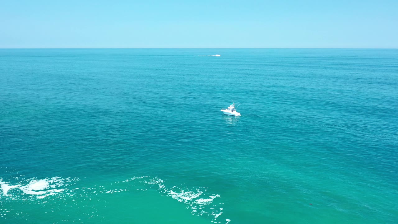 Distant white boat over layered blue ocean and white wave foam