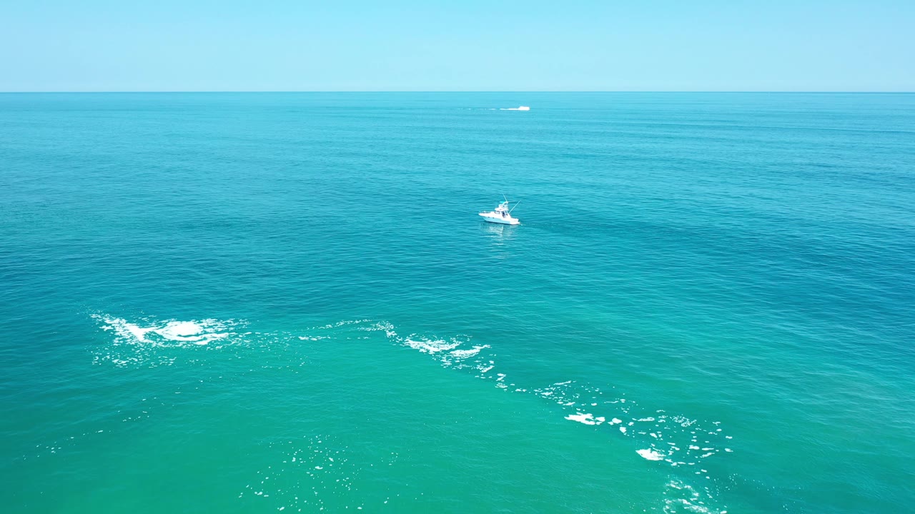 Boat on open turquoise sea with white ripples and clear horizon.