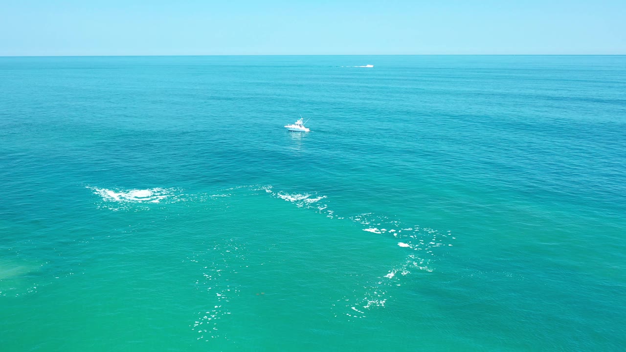 Teal ocean water with distant boats and white foam patches