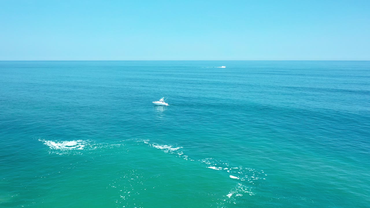 Small white boat on blue ocean with white water patches below.