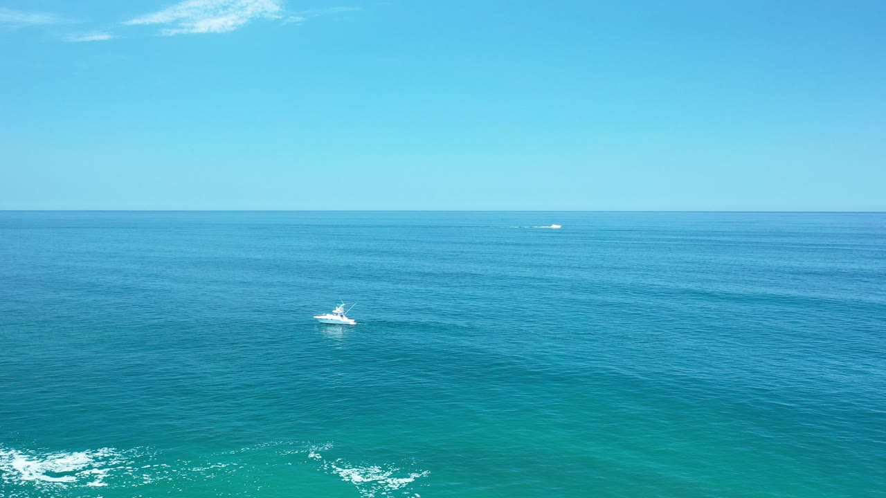 Wide blue ocean with a small boat and distant horizon.