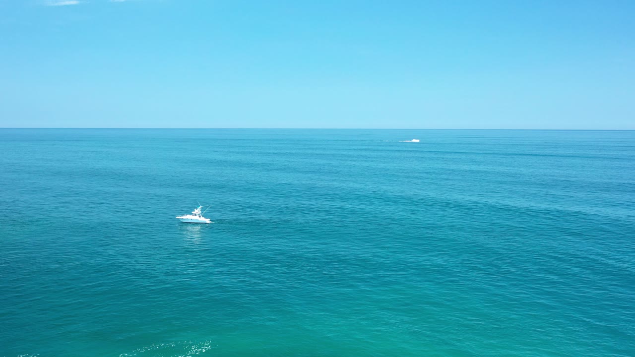Small white yacht on turquoise ocean under a clear horizon.