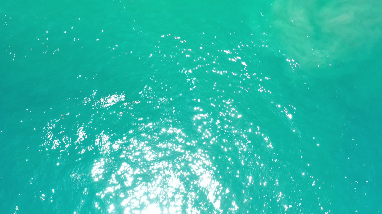 Turquoise water surface with bright sun reflection and small ripples.