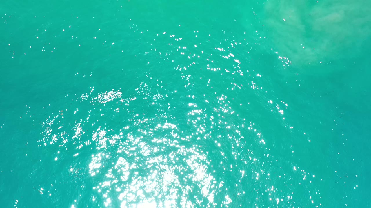 Turquoise seawater in Los Cabos, Mexico, fills the frame with the sun glare shifted near the lower center and no visible people.