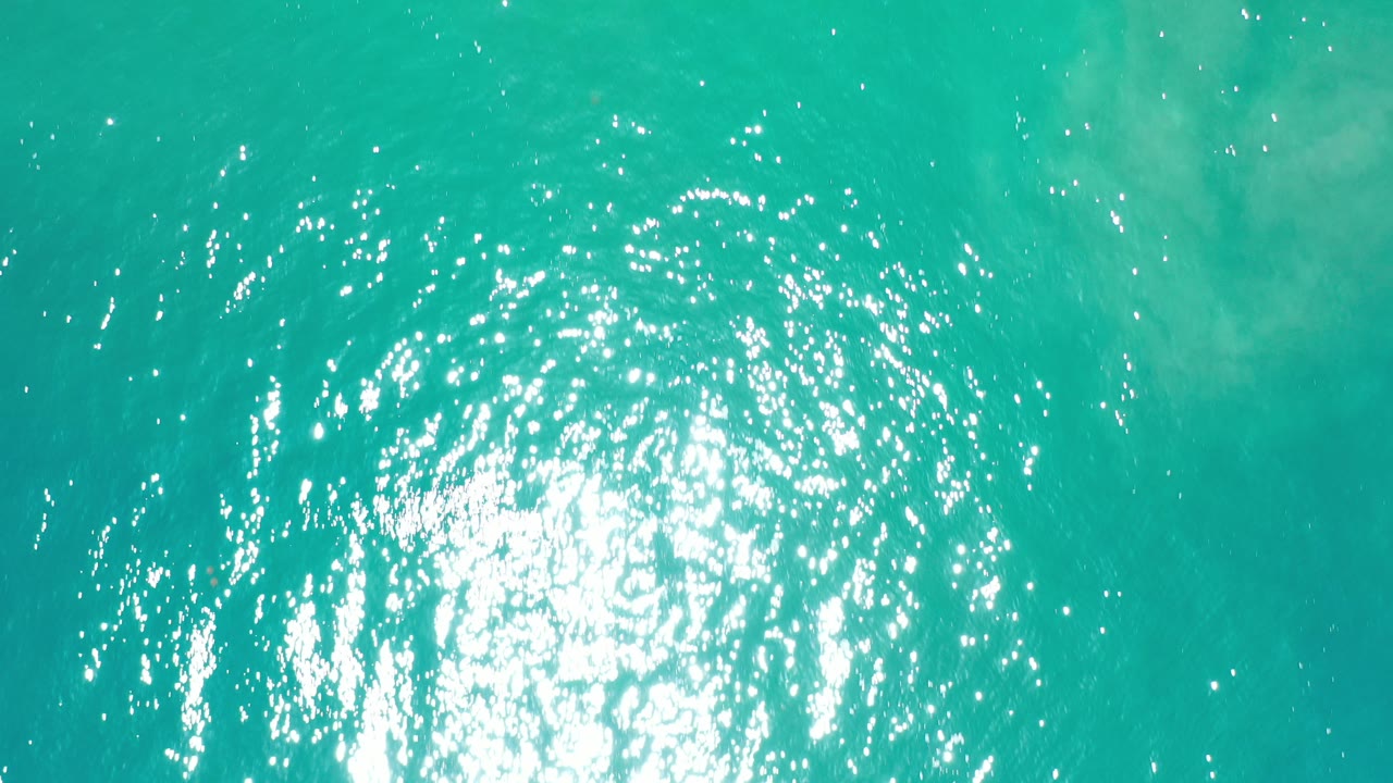 Overhead turquoise ocean water with bright sun reflection.