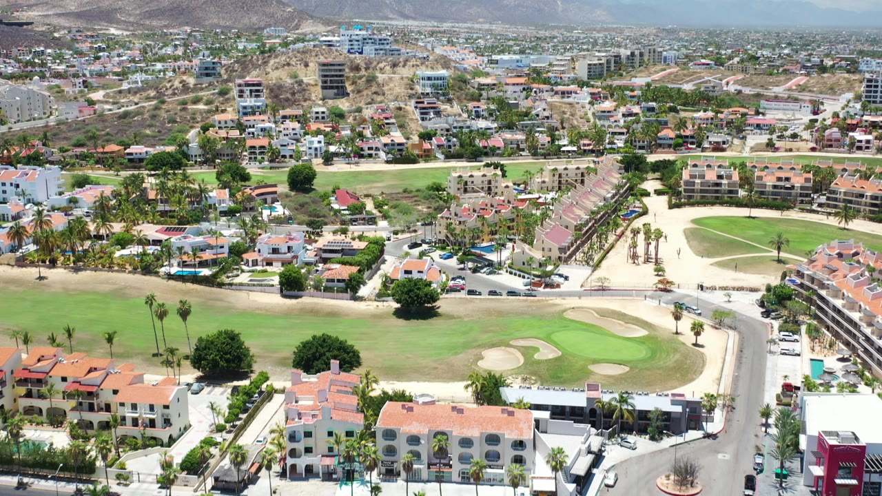 Aerial view of golf course, homes, city blocks, and mountains.
