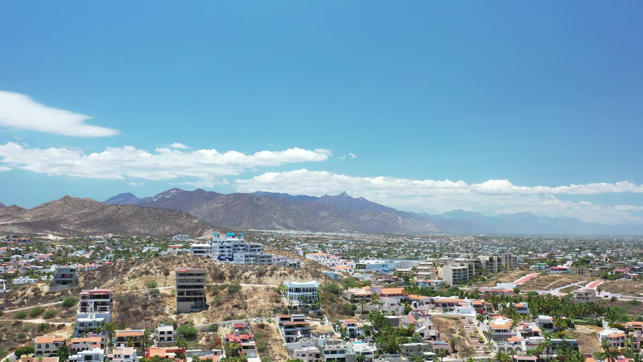 Town and hotel buildings spread across hills below a mountain range.
