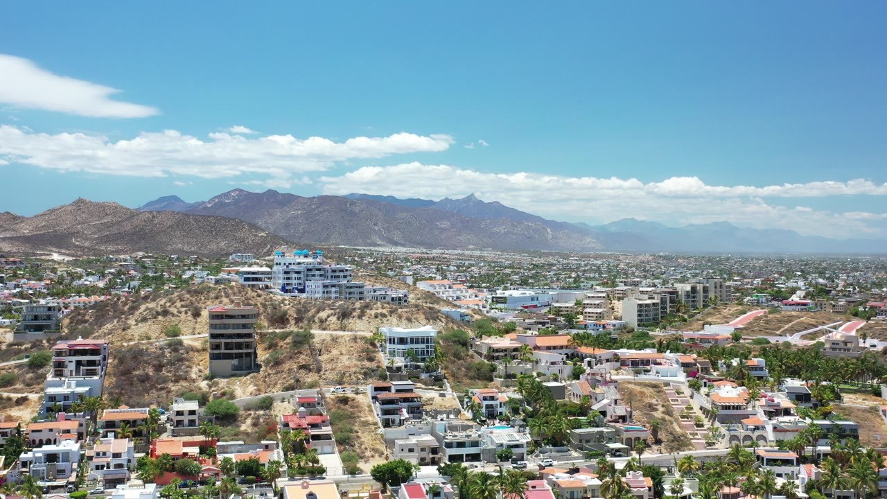 Aerial view of hillside homes, city blocks, and mountains under blue sky.