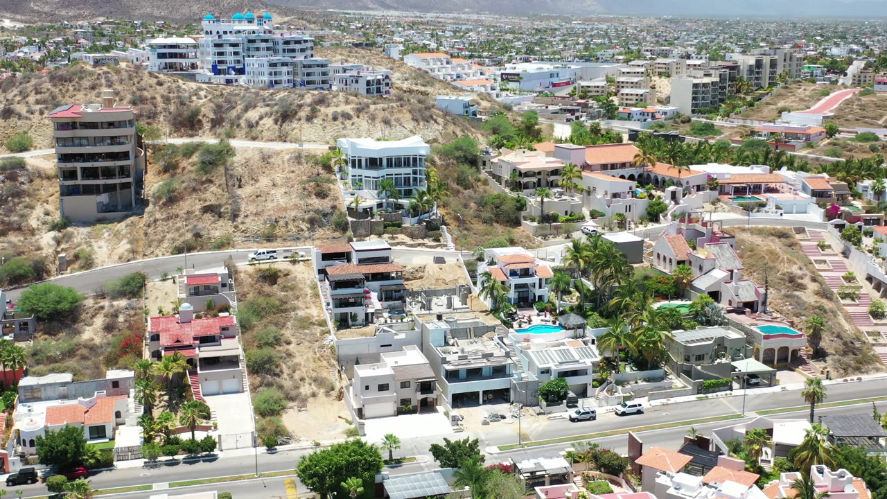 Aerial view of hillside homes, roads, palms, and modern buildings.
