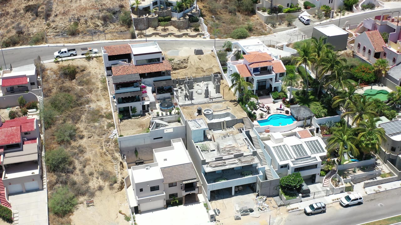 Overhead angle on homes, pool, palm landscaping, and hillside road.