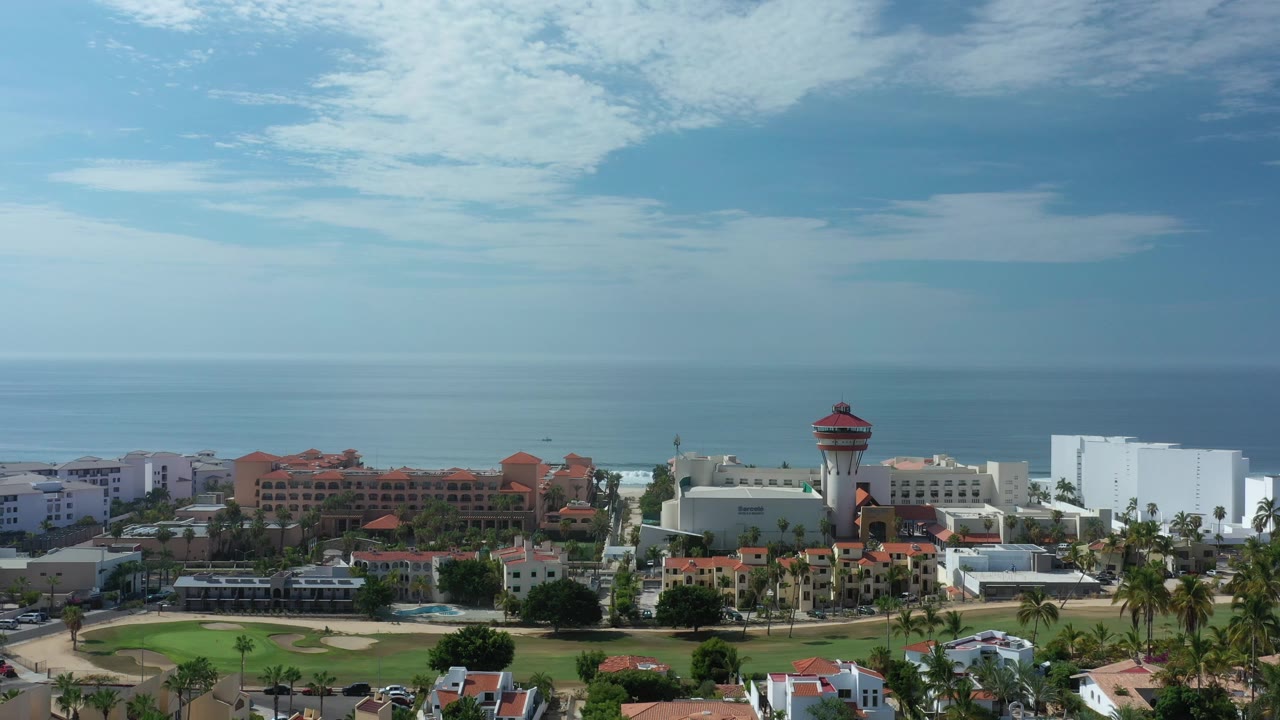 Coastal resort buildings and palms under a large blue sky