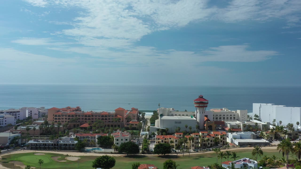 Aerial view of coastal buildings, beach, ocean, and cloudy sky.