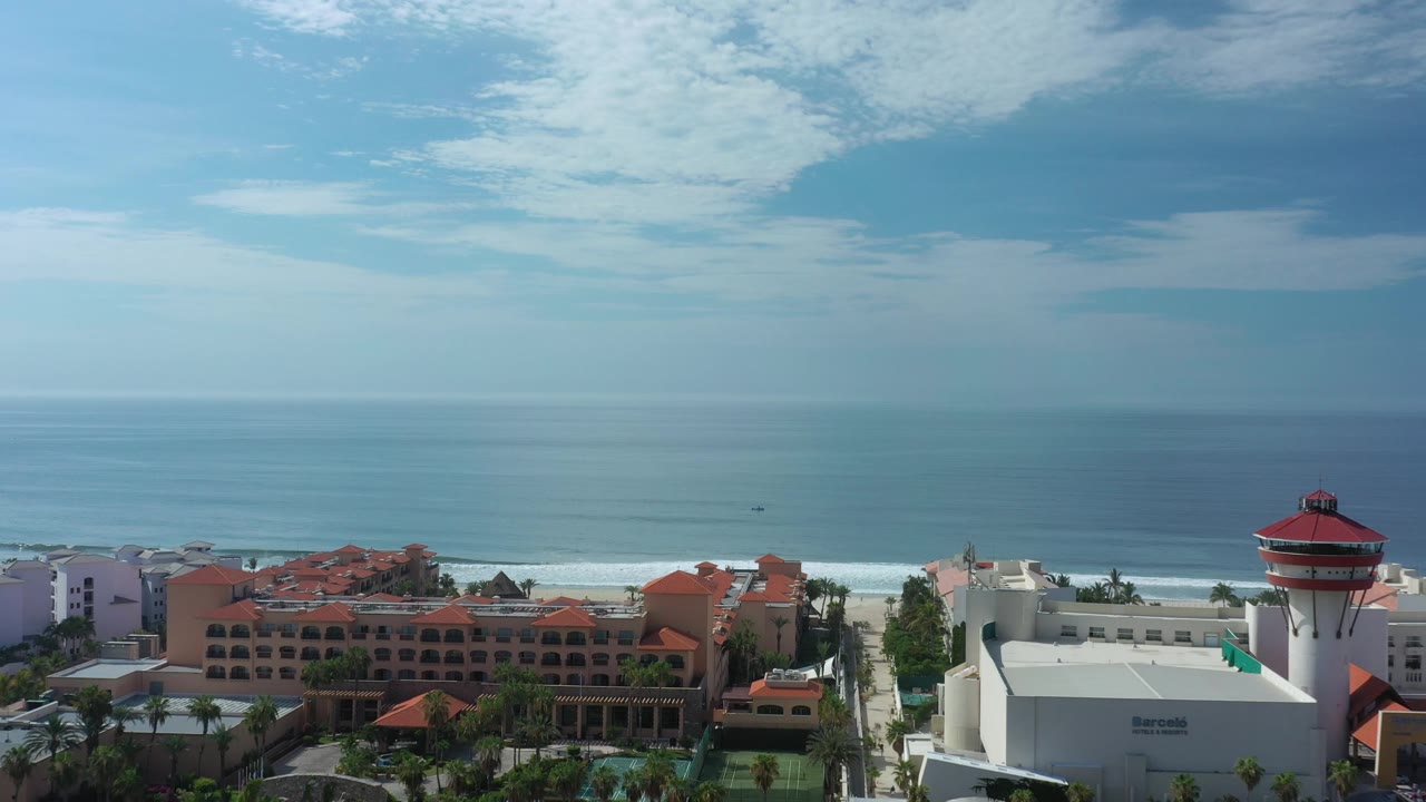 White coastal building and tower beside red-roofed hotels with ocean beyond.