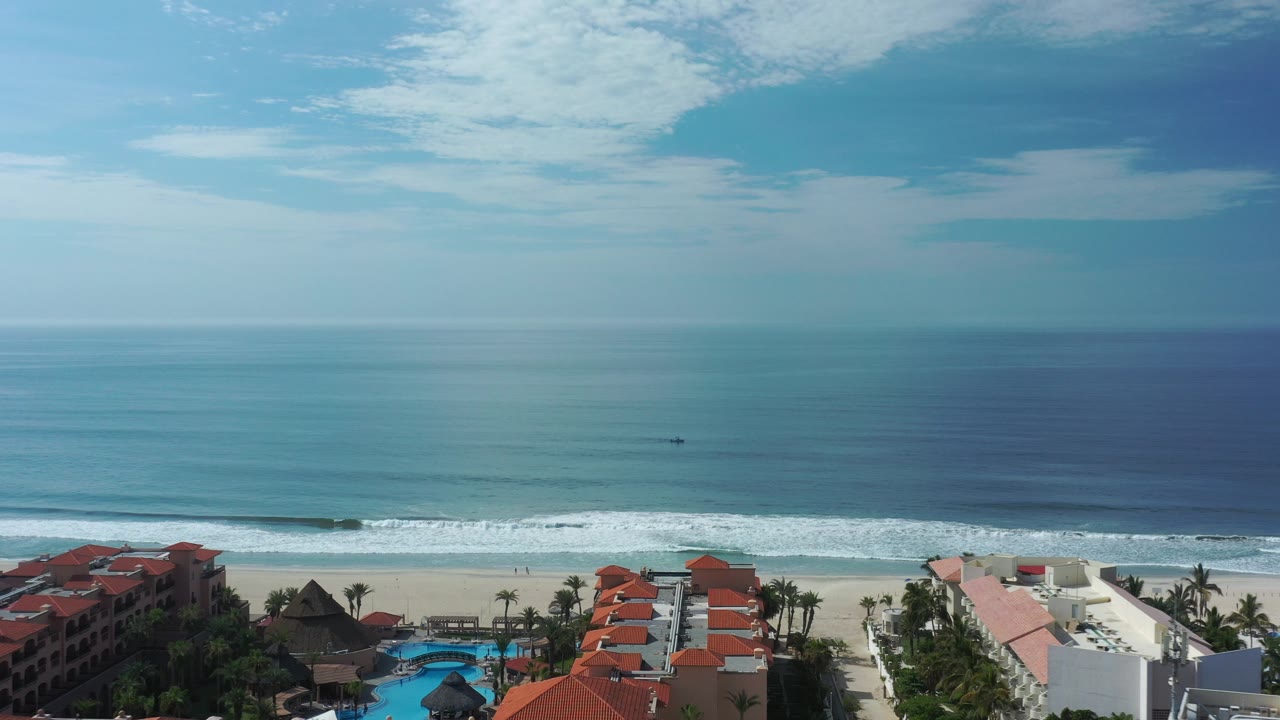Wide coastal view over resort rooftops, beach, surf, and ocean.