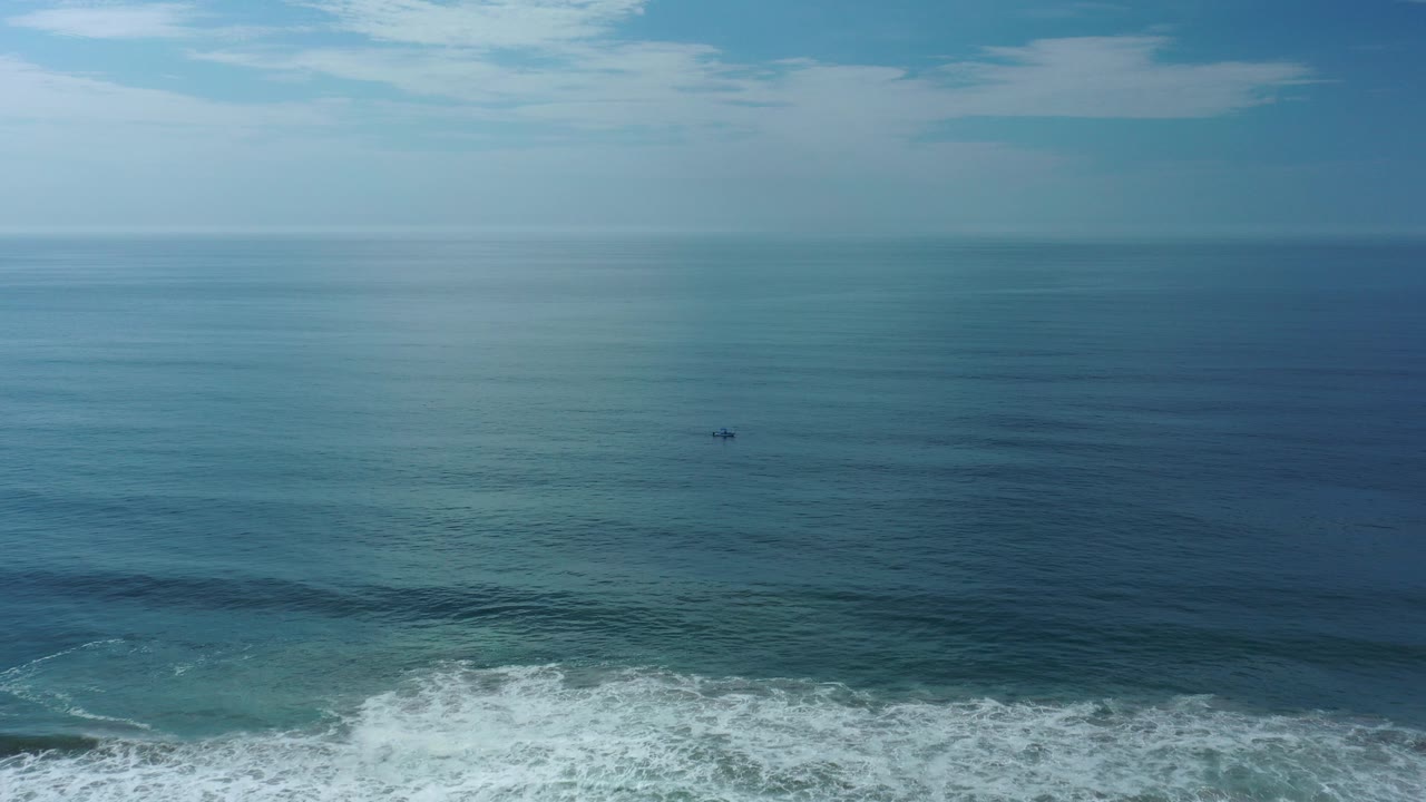 Los Cabos ocean view with white surf along the lower frame, a small distant boat on blue-green water, a level horizon, and no visible people.