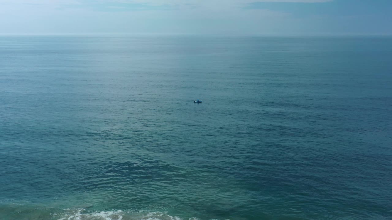 Aerial frame over open water near Los Cabos, Mexico, showing a small dark subject against soft ripples and a pale horizon band.