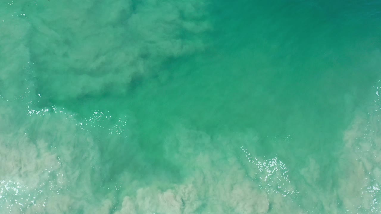 Overhead view of green water and pale foam over sandy shallows in Los Cabos, Mexico, with no visible people.