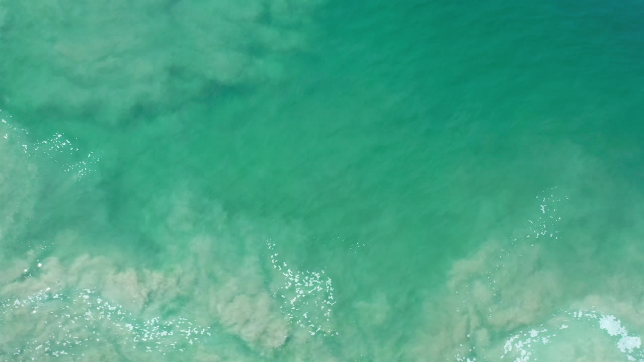 Aquamarine water with tan underwater sand and foam patches.