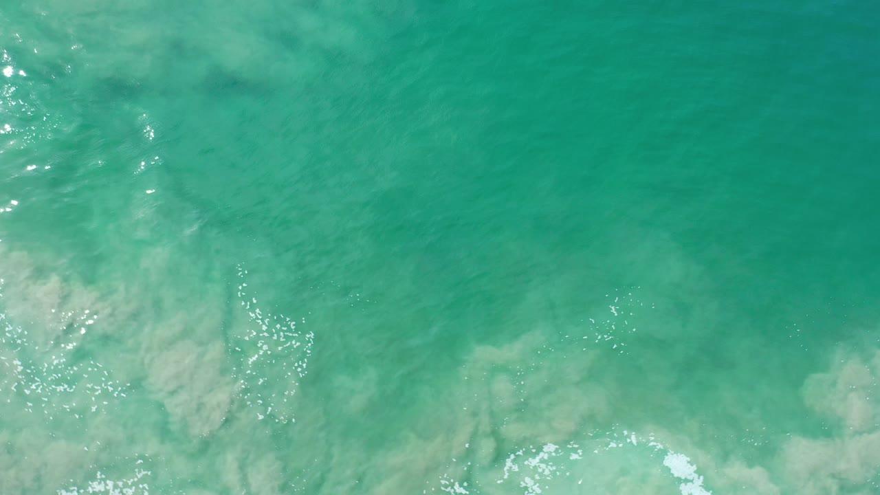 Overhead view of green-blue sea water in Los Cabos, Mexico, with pale underwater shapes, small white foam near the lower edge, and no visible people.