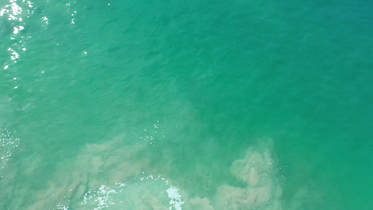 Green-blue ocean surface with underwater pale patches and foam at the bottom.