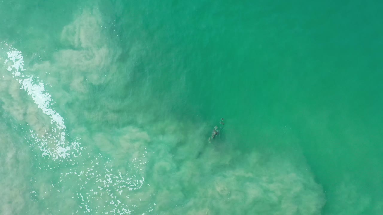 Overhead turquoise ocean water with bright reflection and pale underwater patterns.