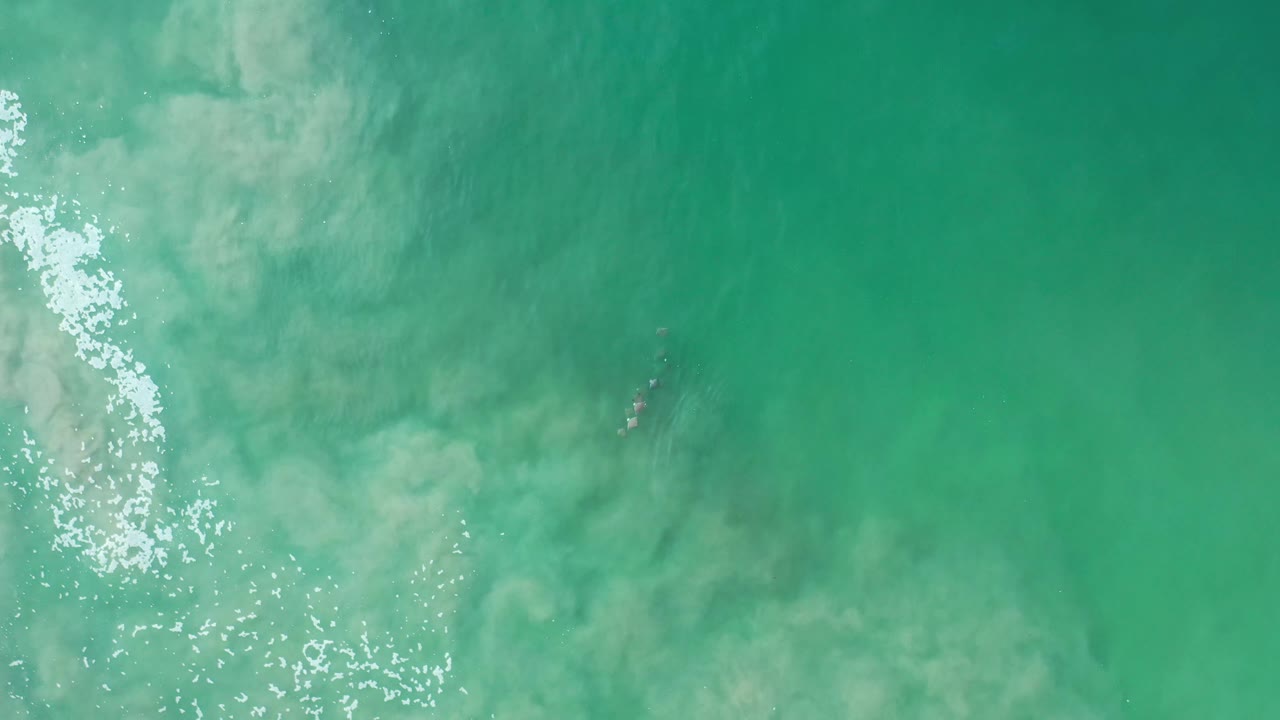 Overhead Los Cabos ocean frame with green-blue water, white sparkle along the left side, a small darker underwater patch, and no visible people.