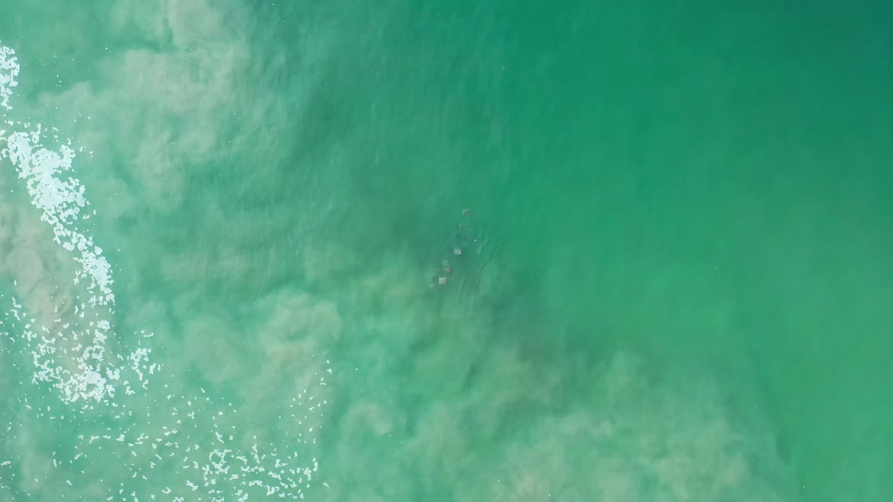 Turquoise sea surface with light foam and clouded shallows.