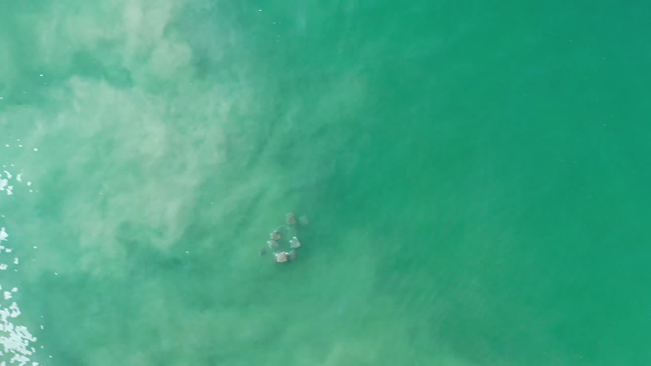 Top-down view of greenish blue water in Los Cabos, Mexico, with pale murky sediment below the surface and no visible people.