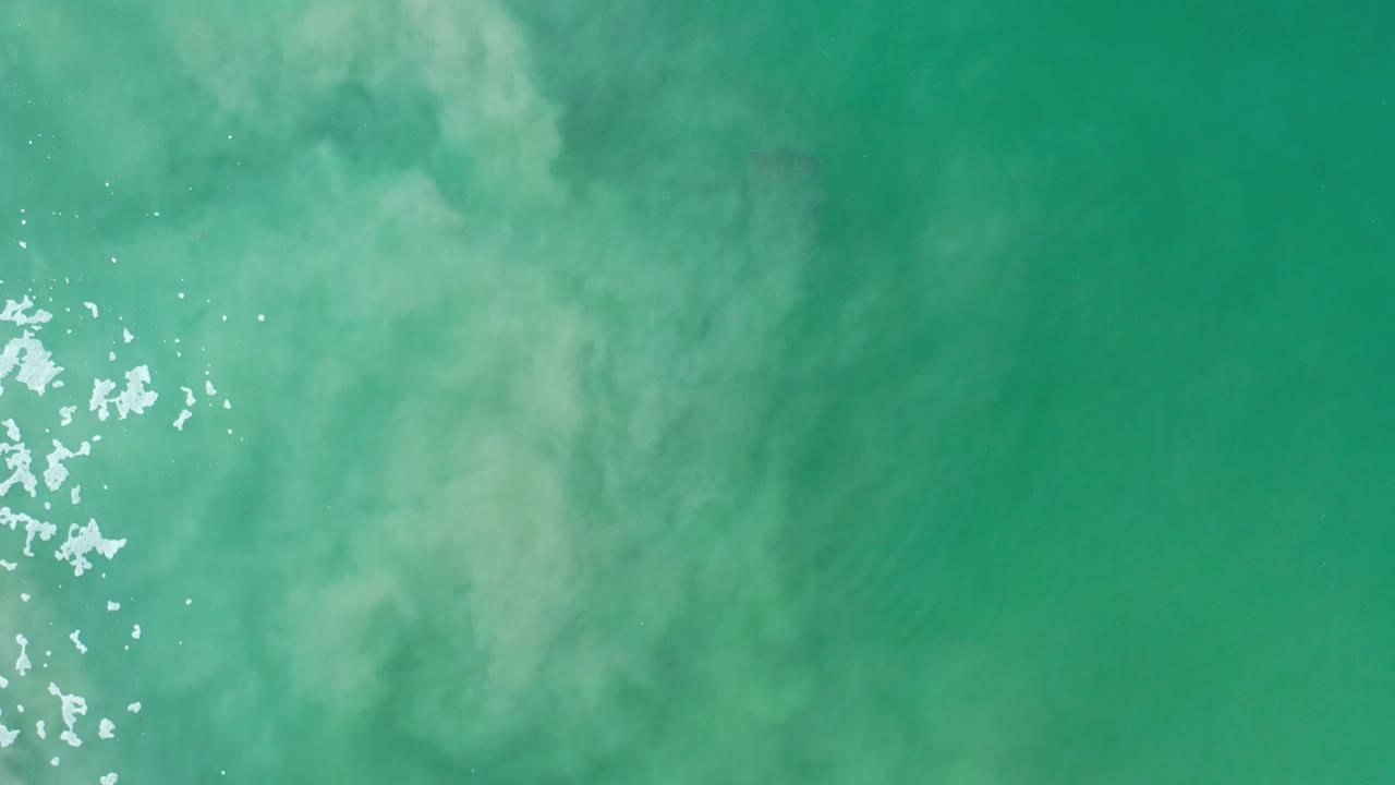 Turquoise-green cloudy ocean water with white surface glints.