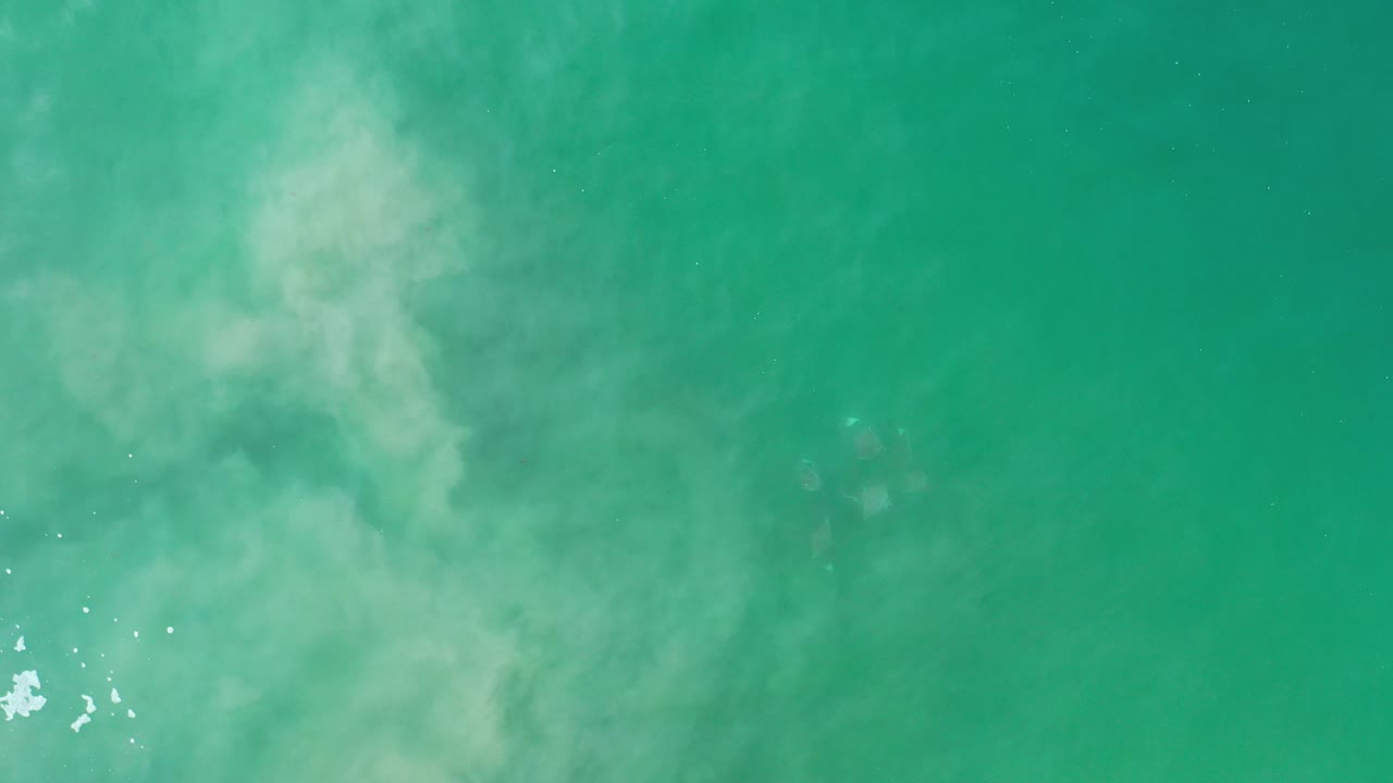 Turquoise water with pale cloudy patches and small white flecks.