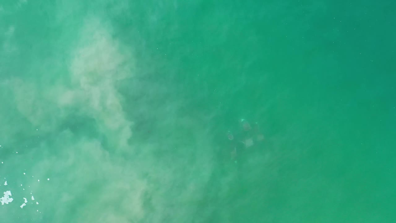 Overhead Los Cabos water frame with a broad pale cloudy patch centered in the turquoise surface and no visible people.