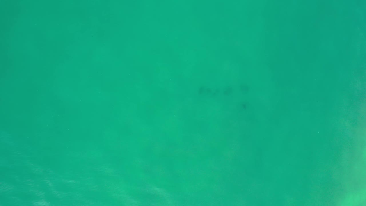 Overhead Los Cabos water frame with turquoise color, cloudy pale sunlit areas, scattered dark specks, and no visible people.