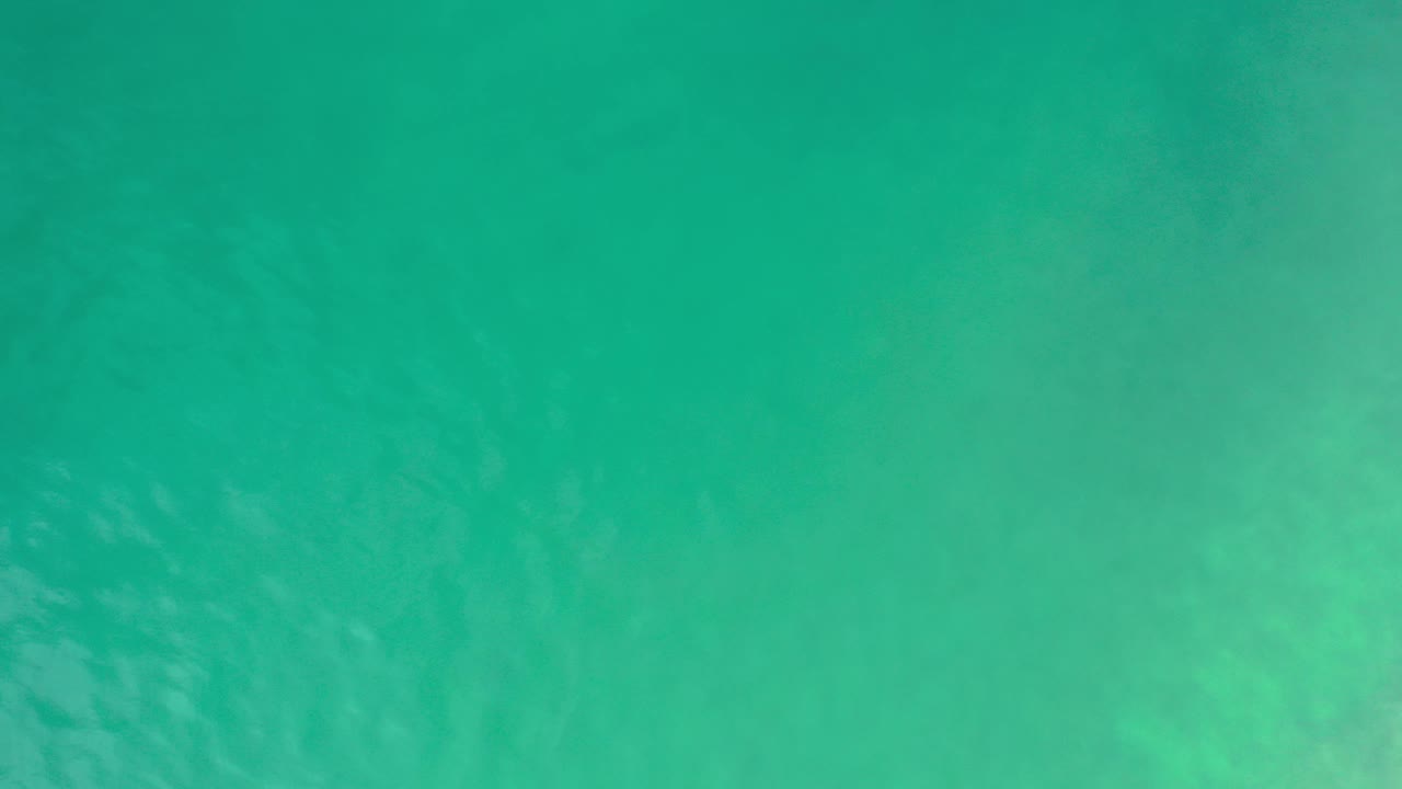Top-down view of turquoise sea water in Los Cabos, Mexico, with faint underwater texture, a tiny dark speck near the left edge, and no visible people.