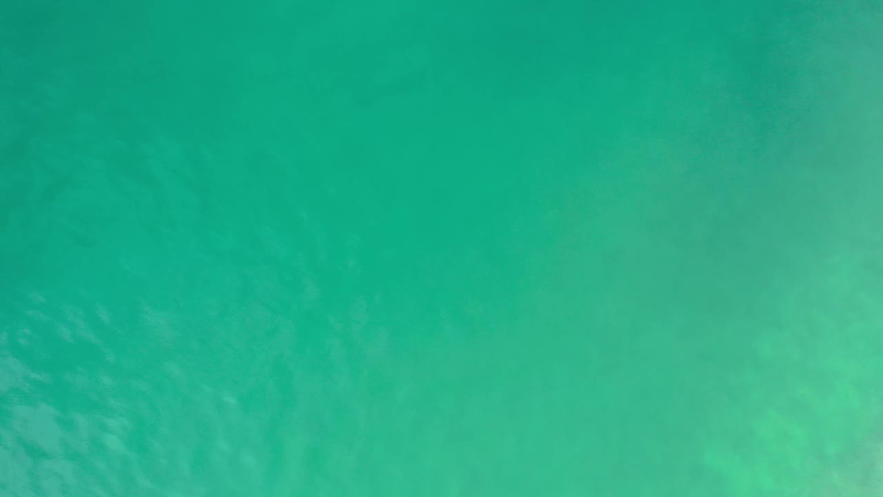 Top-down Los Cabos sea water fills the frame with pale cloudy sand or swell patterns beneath the turquoise surface and no visible people.