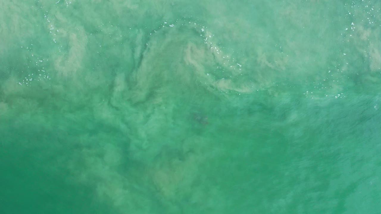 Overhead view of turquoise shallow ocean in Los Cabos, Mexico, with pale sand patterns under the water and no visible people.